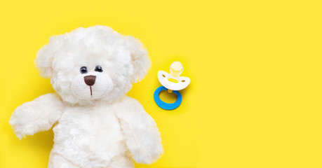 Baby pacifier with toy white bear on yellow background.