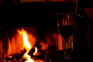 Bottle and glass with wine in the foreground and the background fireplace with high flames.