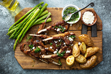 Grilled lamb chops with green herb sauce, feta, asparagus and potatoes served on a wooden board © fahrwasser