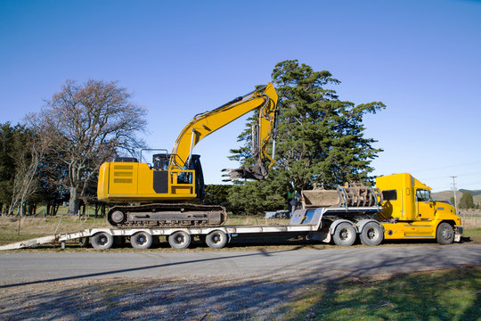 A large yellow digger is delivered to a worksite by a truck and tailer unit in Canterbury, New Zealand