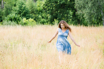Naklejka na ściany i meble girl with beautiful long hair in a blue dress walks across the field