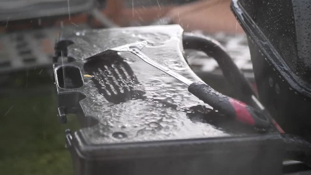 Rain falling on a metal spatula during a rain storm on a black barbecue grill, in slow motion 4k.