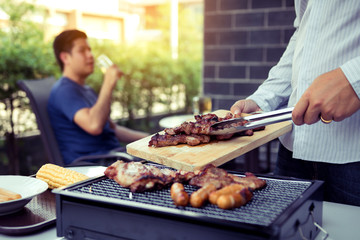 Asian men are pinching pork on a wooden cutting board and holding it to friends who are celebrating in the back.