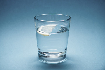 Glass of water with a piece of lemon on a blue background
