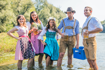 Freunde in bayerischen Tracht feiern an der Isar und trinken Bier. Oktoberfest München
