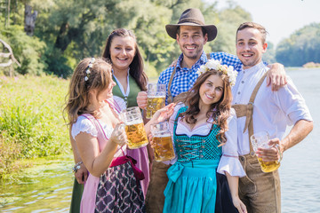 Freunde in bayerischen Tracht feiern an der Isar und trinken Bier. Oktoberfest München