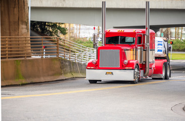 Naklejka premium Classic stylish big rig red semi truck transporting cargo on flat bed semi trailer running under the bridge