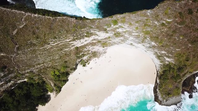 Drone Shot flying over the ridge line separating KelingKing beach and some rugged cliffs of Nuse Penida. Waves can be seen crashing fiercely on both sides of the ridge.