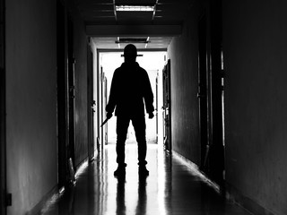 Man silhouette walking away with knife in the light of opening door in dark room, Threat Concept.