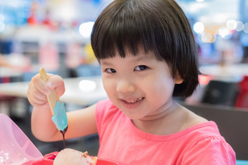 Little girl wear pink shirt and short hair eating ice cream with chocolate topping on bowl, hold spoon and sitting on the chair and table at home, fun, smile and happy, close up photo.