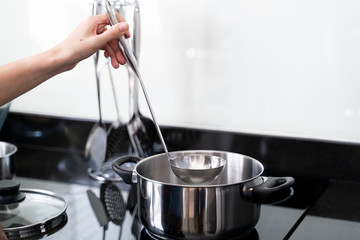 hand holding a ladle or kitchen spoon above pan