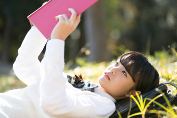 公園で寝転んで読書をする女子校生