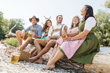 Freunde in bayerischen Tracht feiern an der Isar und trinken Bier. Oktoberfest München