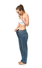 Happy young woman in loose jeans on white background. Weight loss concept