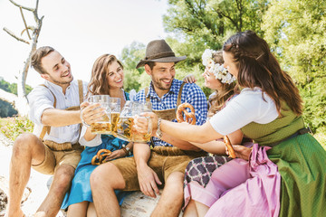 Freunde in bayerischen Tracht feiern an der Isar und trinken Bier. Oktoberfest München