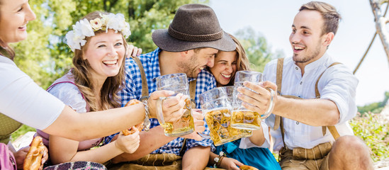 Freunde in bayerischen Tracht feiern an der Isar und trinken Bier. Oktoberfest München