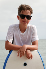young man with sunglasses on the beach leaning on boogie board.