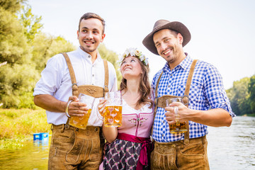 Freunde in bayerischen Tracht feiern an der Isar und trinken Bier. Oktoberfest München