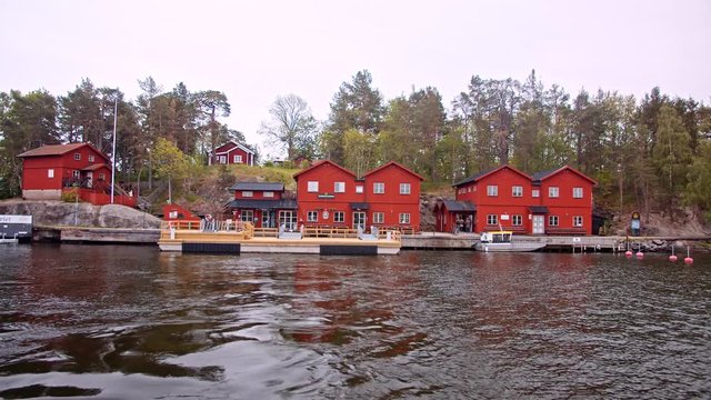 Small marina with calm waters and traditional red painted houses in background, on the Stora Fjäderholmen island, in the Fjäderholmarna archipelago, near Stockholm, Sweden.