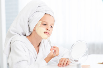 Young girl in towel on her head  make a clay facial mask at home