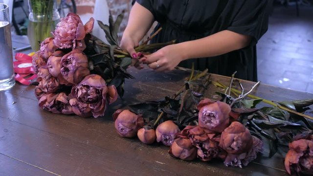 Floral business concept. Florist woman works makes bouquet of brown maroon color peonies in flower shop for sale, hands closeup. She creates professional bunch composition in floristic studio store.