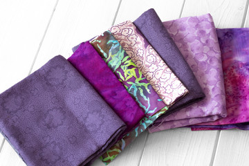 Various fabric material sample swatches,  with a purple theme, on a white wood background
