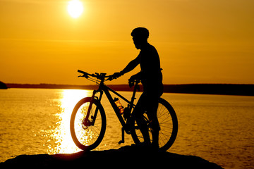 Fototapeta premium Silhouette of sportsman riding a bicycle on the beach. Colorful sunset cloudy sky in background