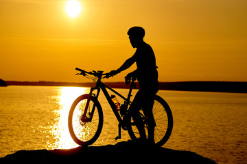 Silhouette of sportsman riding a bicycle on the beach. Colorful sunset cloudy sky in background