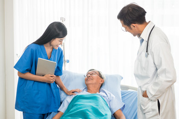 Doctor and physiotherapist talking to elderly patient lying on bed