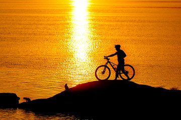 Fototapeta premium Silhouette of sportsman riding a bicycle on the beach. Colorful sunset cloudy sky in background.