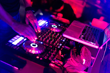 A DJ is using music mixer in the nightclub with colorful light