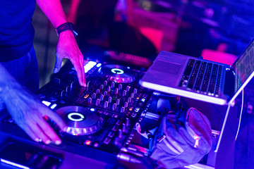 A DJ is using music mixer in the nightclub with colorful light