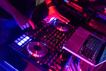 A DJ is using music mixer in the nightclub with colorful light