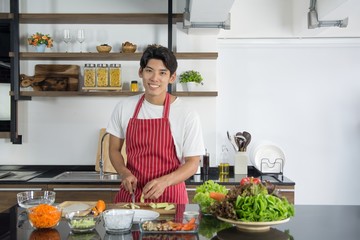 Man in red apron cooking delicious and healthy food in the loft kitchen on sunny day. Preparing vegetable salad
