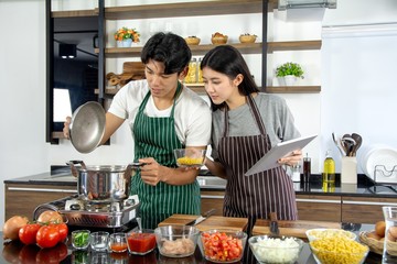 Portrait of cute happy couple in apron in selfie action holding tablet and cereal preparing cooking brekafast decorated with salad in modern kitchen