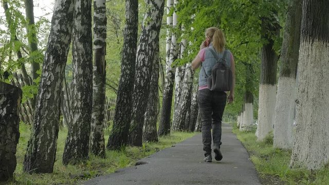 The girl is in the park on the wet asphalt after the rain.