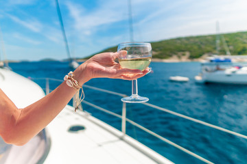 Woman holding glass of white wine over ocean background with yacht on background