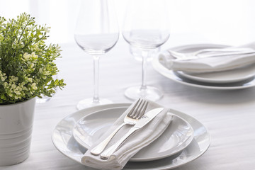 Table setting white and grey colour. Empty glasses and plates set with napkin and cutlery. Restaurant interior background...