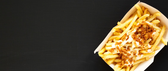 Overhead view, french fries with cheese sauce and onion in a paper box on a black background. Flat...