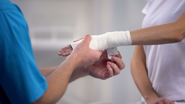 Orthopedist applying wrist elastic wrap on female patient hand joint dislocation