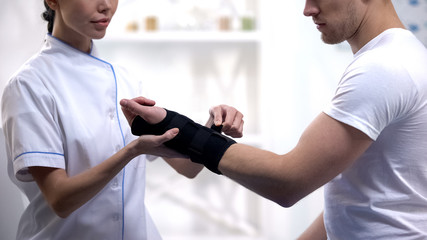 Nurse fixing wrist support to male patient, joint inflammation, rehabilitation