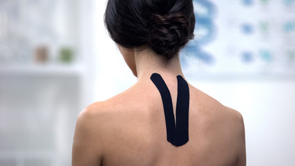 Fototapeta na wymiar Woman with Y-shaped tape on upper back, reducing pain, alternative medicine