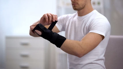 Sportsman fixing titan wrist support, inflammation or sprain, orthopedics - obrazy, fototapety, plakaty