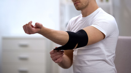 Young male applying elbow padded orthosis, orthopedics and physiotherapy, health