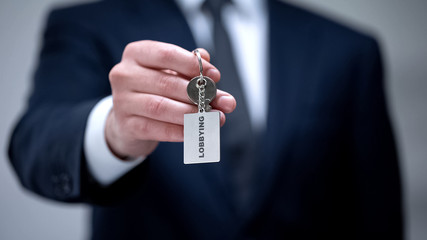Lobbying word on keychain in businessman hand, illegal protection of interests