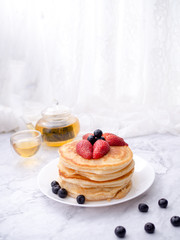 Stack of pancakes with topping, strawberry and blueberry.Placed in a white plate on a marble table and copy space.Eat with tea in the glass.