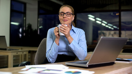 Happy businesswoman enjoying fragrant aroma of coffee, having break from work