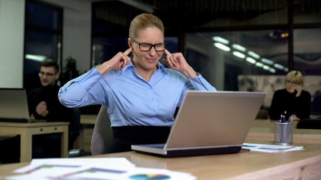 Irritated lady closing ears with fingers, noisy colleagues distracting from work