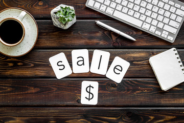 Sale in shop office with word and dollar sign, keyboard, notebook on wooden background top view