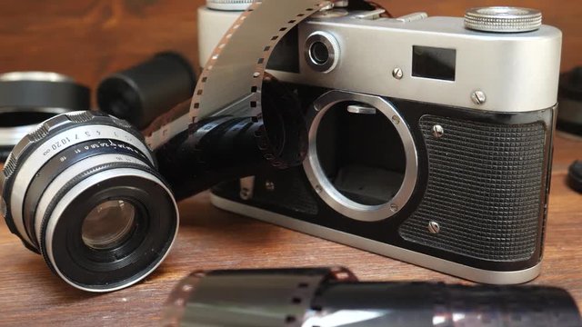 Retro photo camera with photographic film and lens on brown wooden background